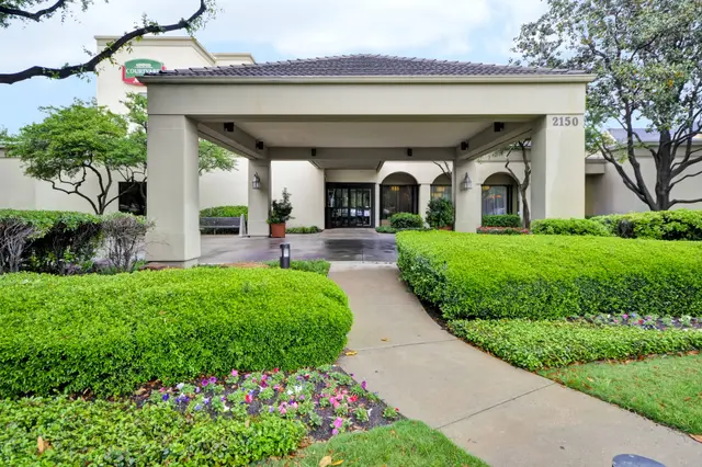 The covered entrance of the Courtyard Dallas Medical/Market Center, with hedges and flower beds.