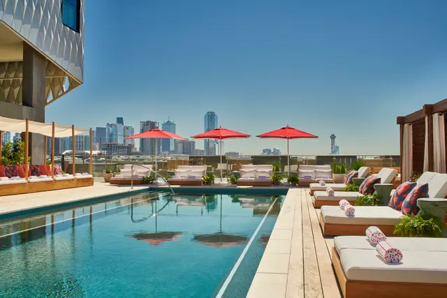 The rooftop pool at Virgin Hotels Dallas, with red umbrellas and the downtown skyline.