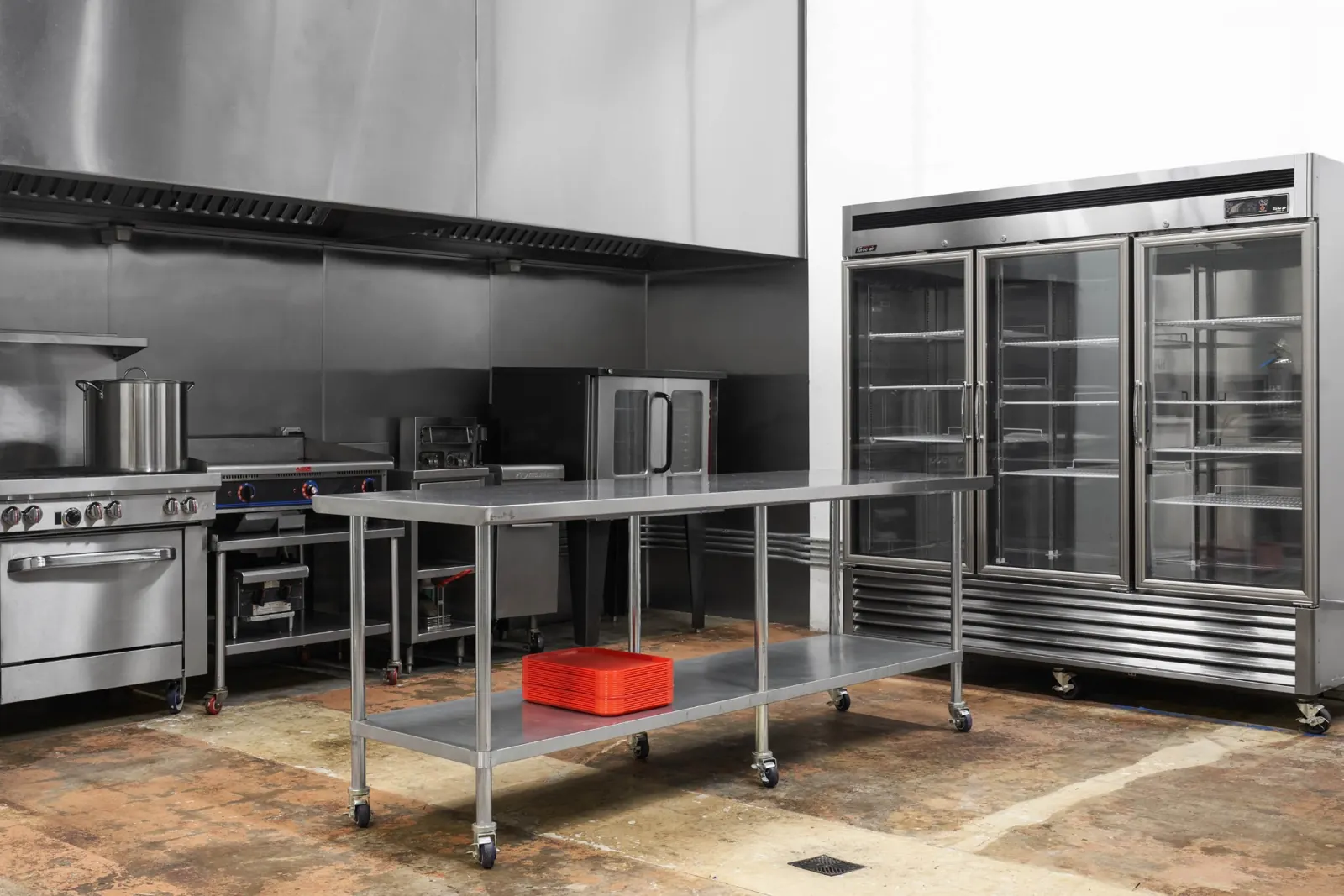 One Monster Prep Kitchen: steel range, prep table, a three-door cooler and one stack of red trays.