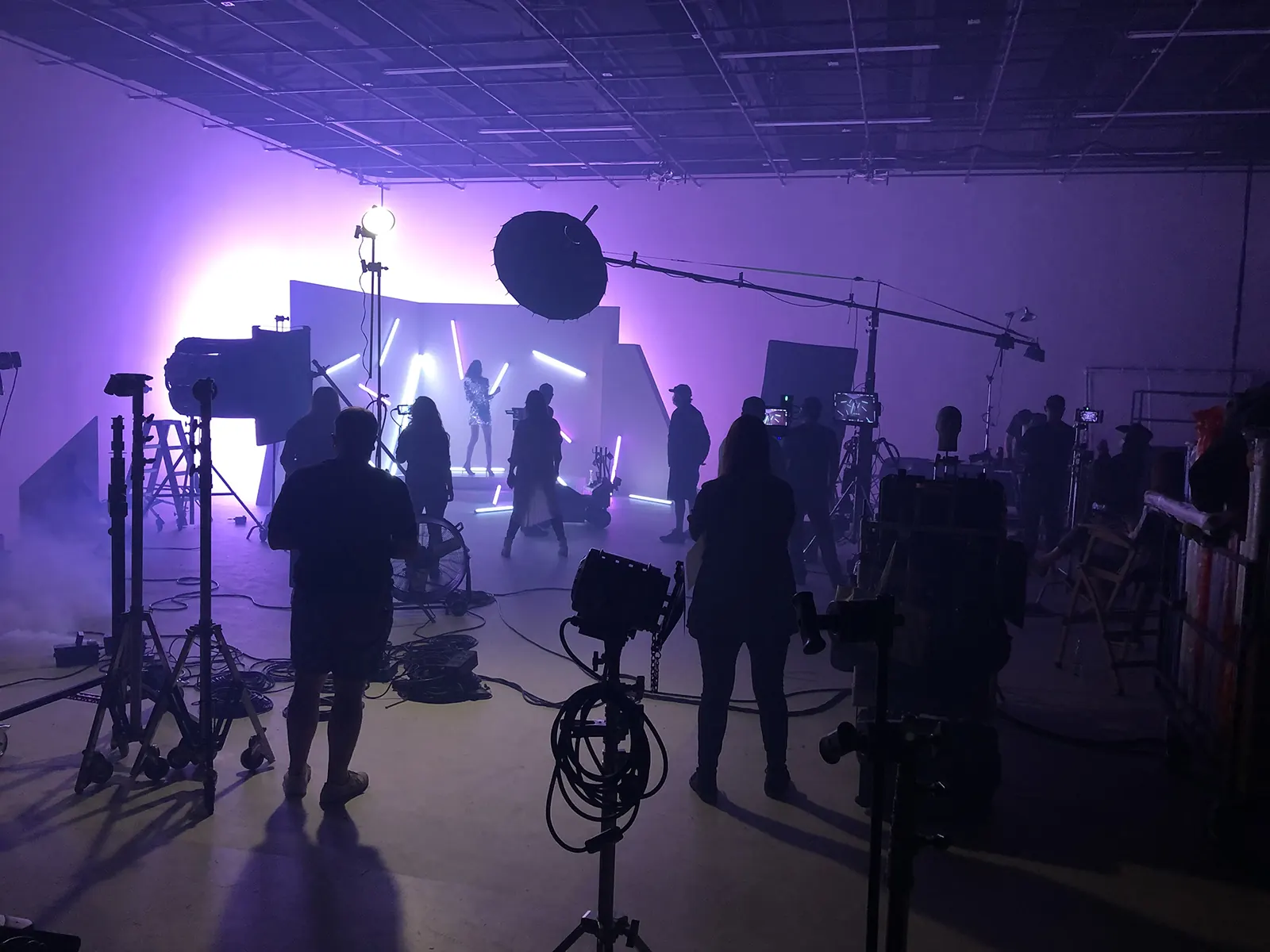 A crew at work on the stage, lit in violet, with cameras and a boom in silhouette.