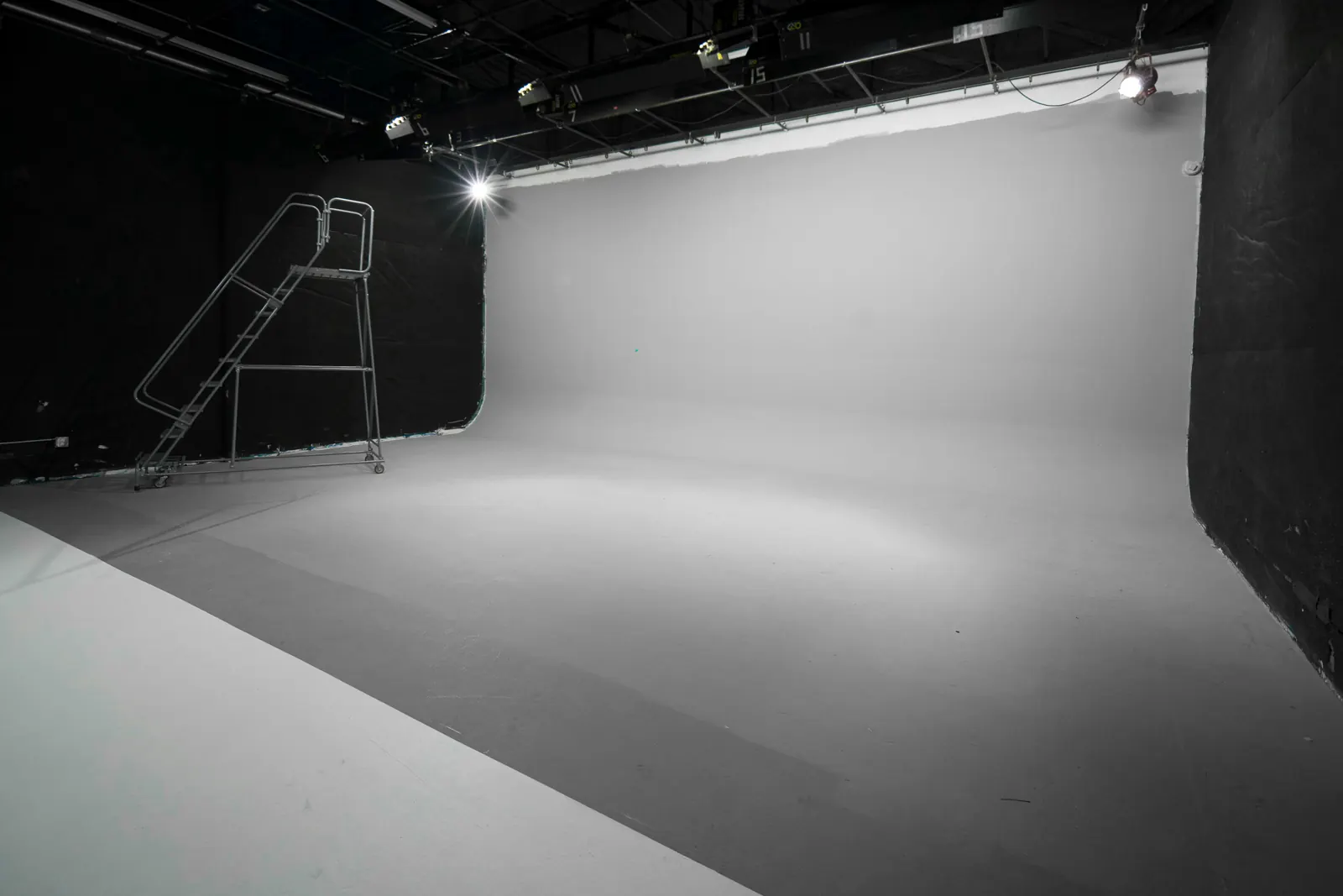 Little Lair: a white cyclorama with a rolling ladder and overhead lights.